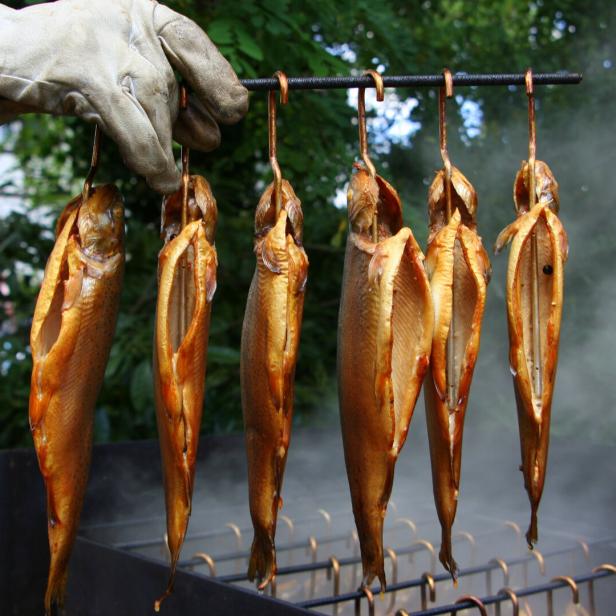 Geräucherte Forellen hängen über einem Grill.