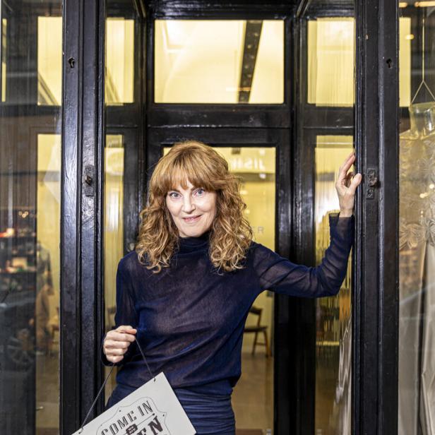 Michaela Mayer hält ein Schild mit der Aufschrift „Come in, we are open“.