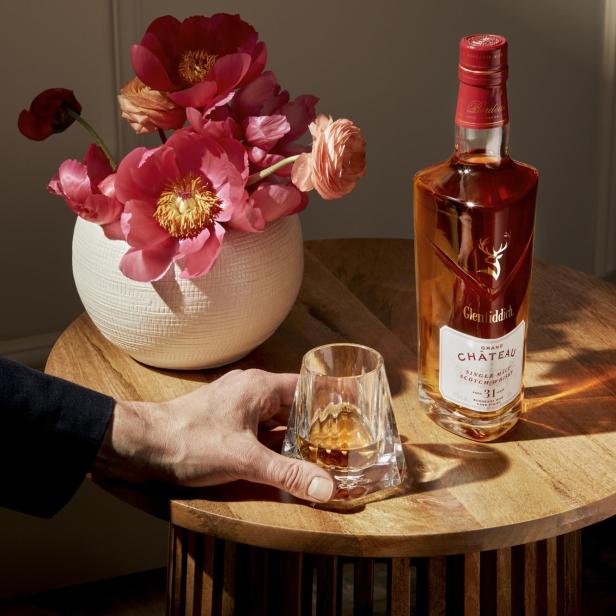 Eine Flasche Glenfiddich Grand Château Whisky neben einem Glas und einem Blumenarrangement.