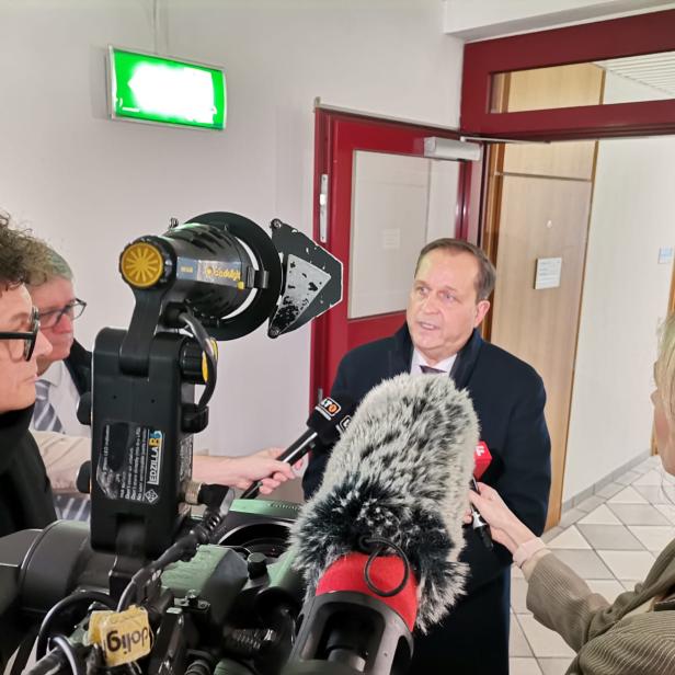 Ein Mann wird von mehreren Reportern mit Mikrofonen interviewt.