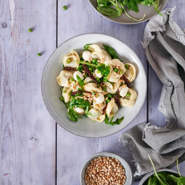 Ein Teller Tortellini-Salat mit Rucola, Erbsen, Mozzarella und Pinienkernen.