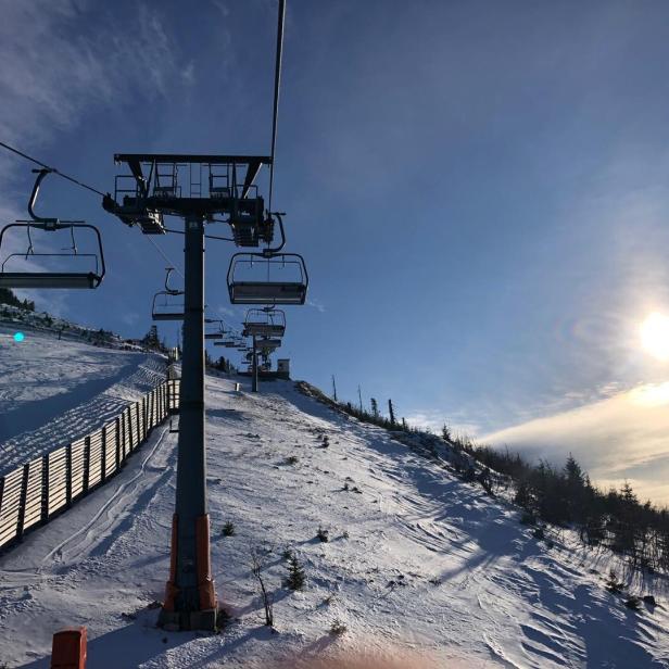 Ein Skilift führt einen verschneiten Hang hinauf, mit blauem Himmel und Sonnenschein.