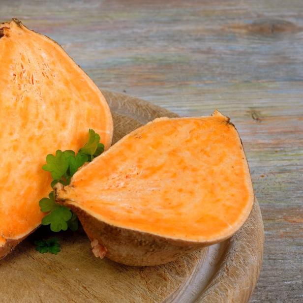 Zwei halbe Süßkartoffeln liegen auf einem Holzbrett.