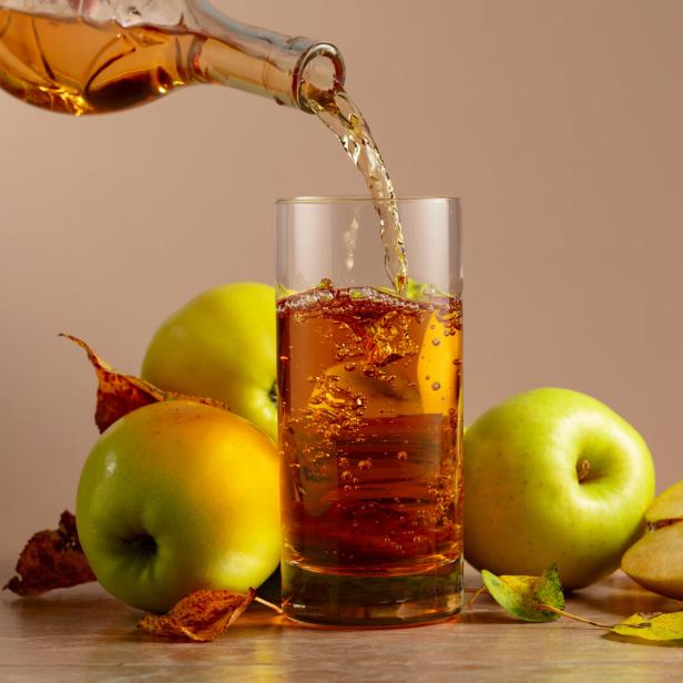 Apfelsaft wird in ein Glas gegossen, umgeben von Äpfeln.