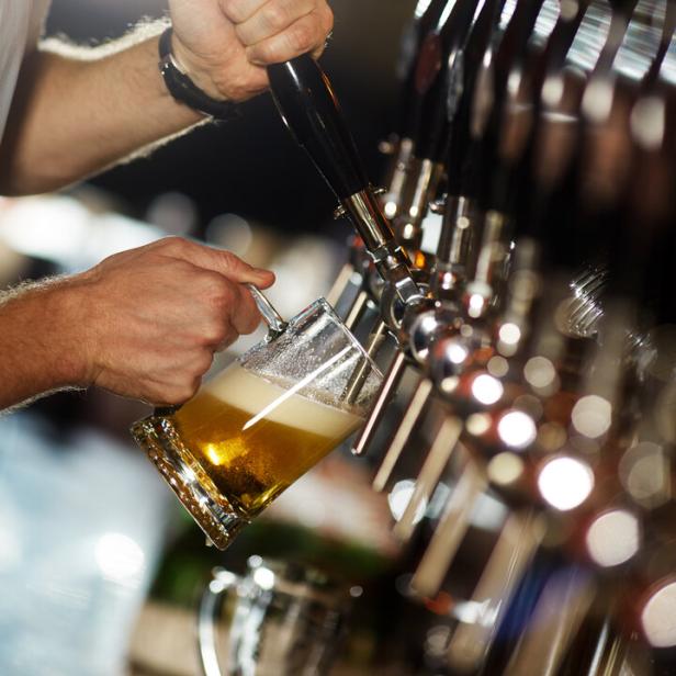 Ein Barkeeper zapft ein Glas Bier an einer Reihe von Zapfhähnen.