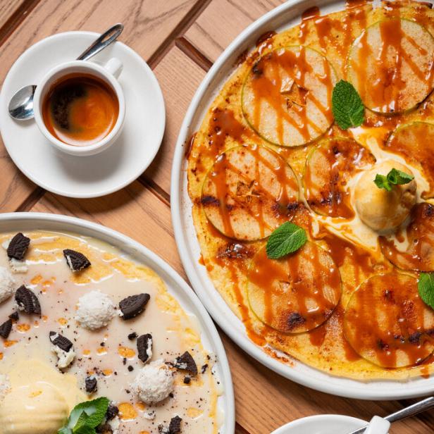 Zwei Teller mit Crêpes, garniert mit Äpfeln, Oreo-Keksen und Kokosraspeln, dazu Kaffee.