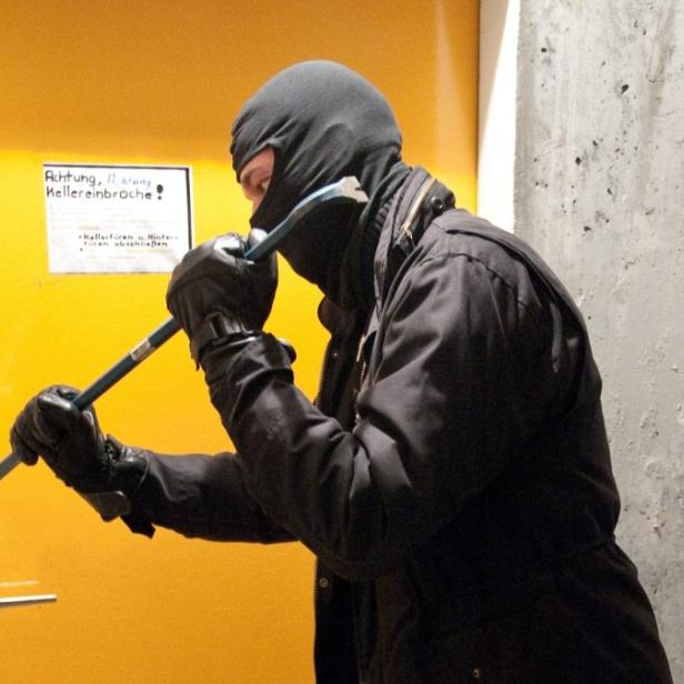 Einbrecher hebelt mit einem Brecheisen eine gelbe Tür auf.