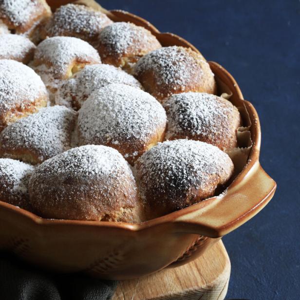 Ein Auflauf mit süßen, mit Puderzucker bestäubten Brötchen und einer Schale Aprikosenmarmelade.