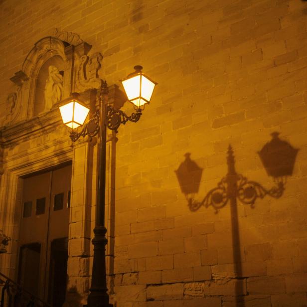 Eine beleuchtete Straßenlaterne vor einer Kirche bei Nacht.