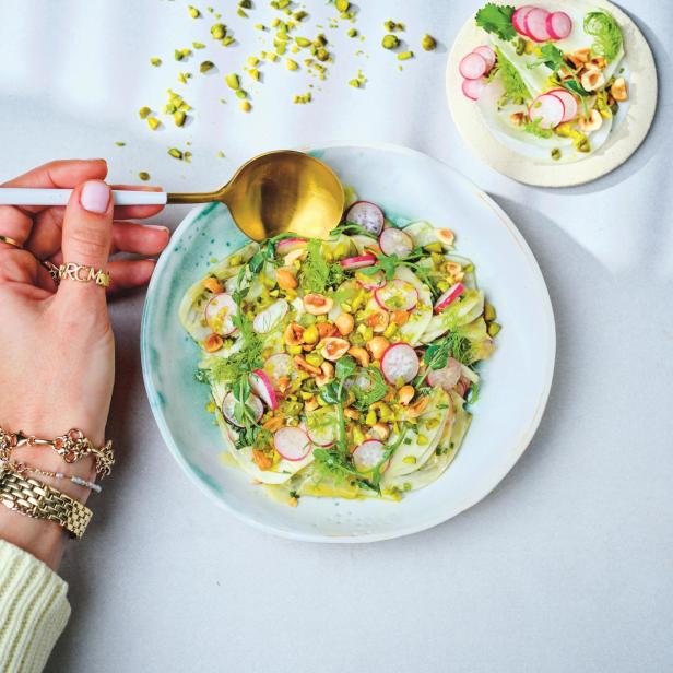 Ein Teller Fenchelsalat mit Radieschen und Pistazien wird mit einem goldenen Löffel serviert.