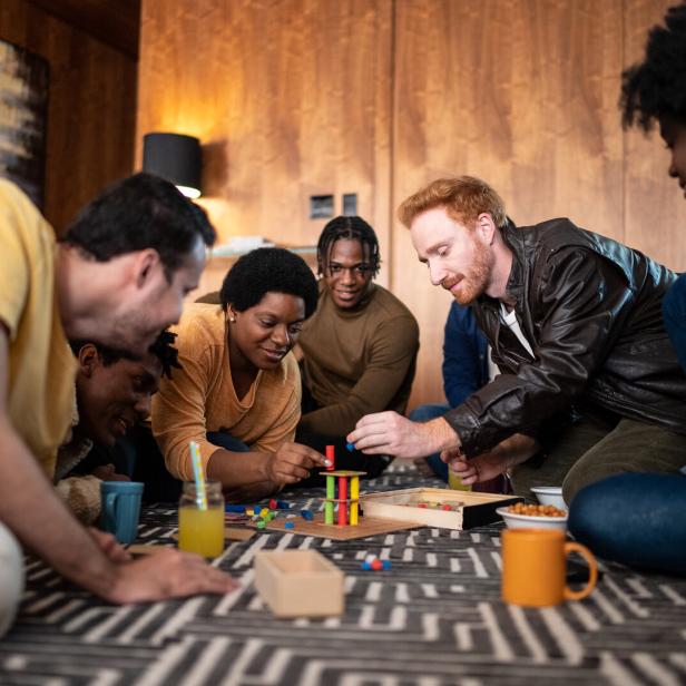 Eine Gruppe von Freunden sitzt auf dem Boden und spielt ein Geschicklichkeitsspiel.