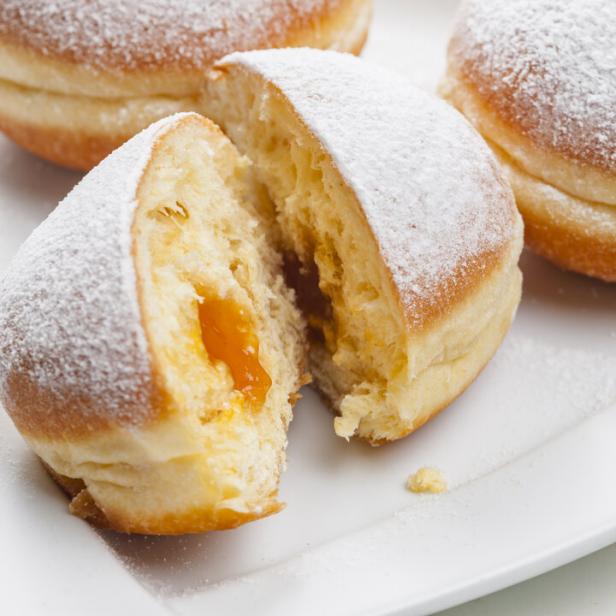 Drei mit Puderzucker bestäubte Marillenkrapfen, einer davon aufgeschnitten.