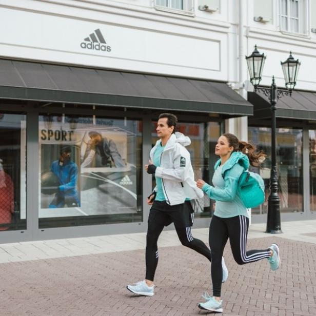 Ein Mann und eine Frau joggen an einem Adidas-Laden vorbei.