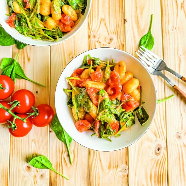 Zwei Schüsseln mit Gnocchi, Spinat und Tomaten auf einem Holztisch.