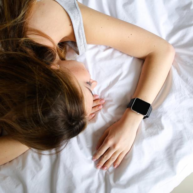 eine Frau liegt schlafend mit einer Smartwatch am Handgelenk im Bett.