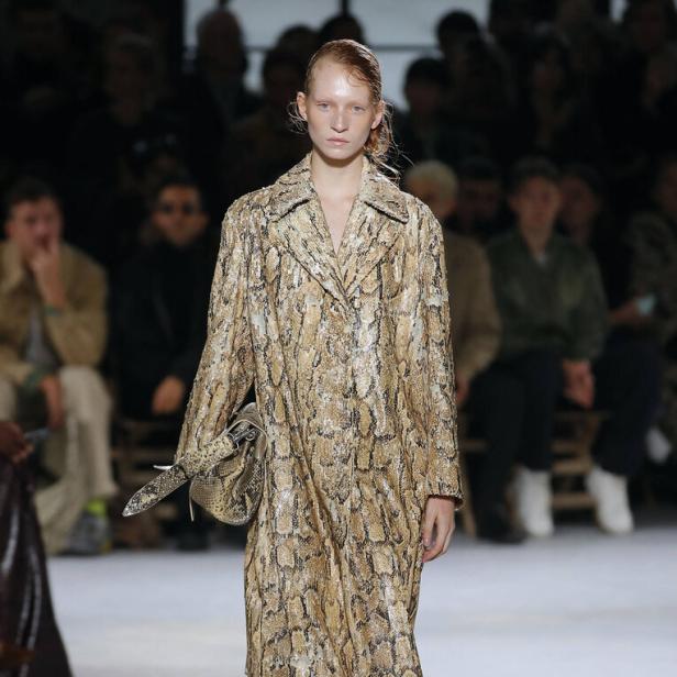 Ein Model auf dem Laufsteg trägt einen Mantel mit Schlangenmuster und rote Schuhe.