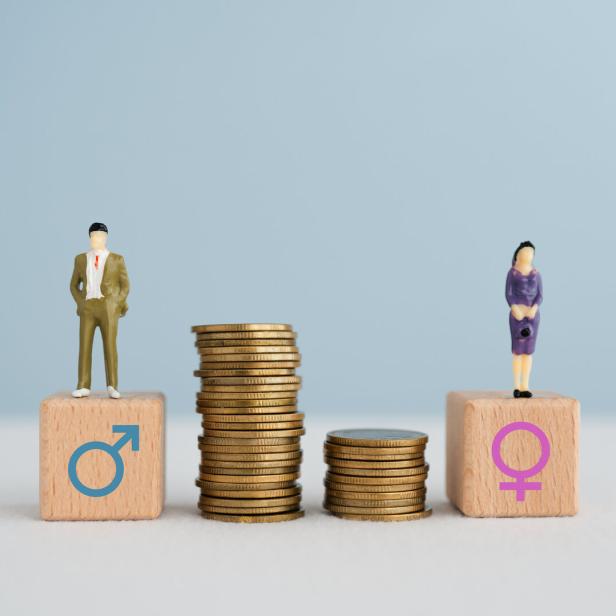Gender pay equality concept. Miniature of man and woman on wooden cube block with stack of coins