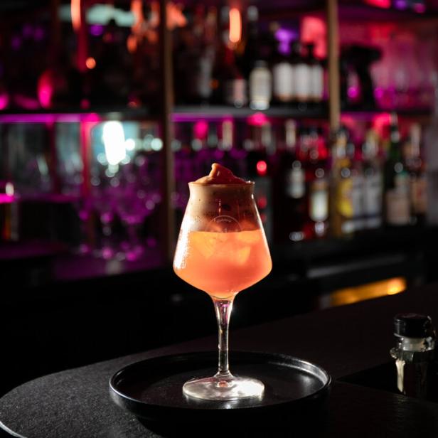 Ein Cocktail mit Eiswürfeln und Schaum steht auf einer Bar.
