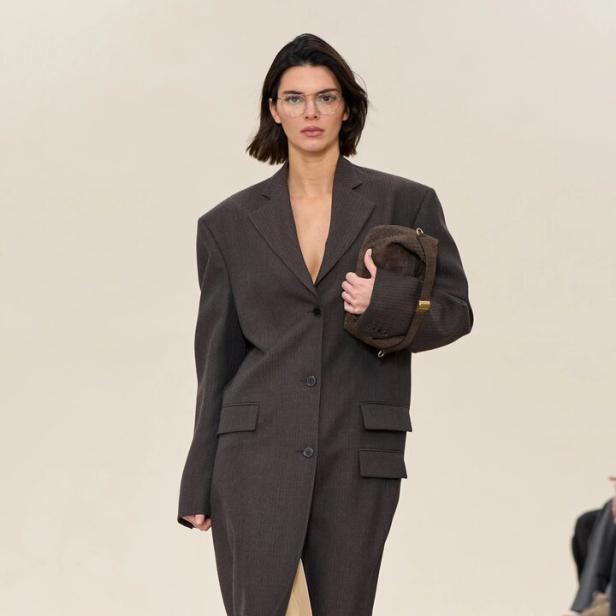 Kendall Jenner trägt einen übergroßen grauen Mantel und eine braune Handtasche auf dem Laufsteg.