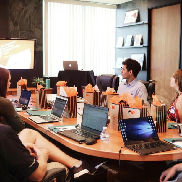 Ein Meeting mit Personen an einem tisch und Laptops und einer präsentierenden Person