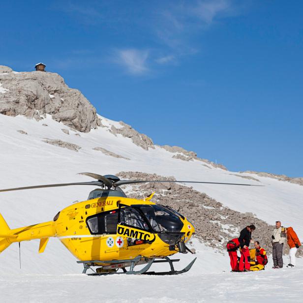 Ein gelber ÖAMTC-Rettungshubschrauber steht im Schnee, während Sanitäter sich um eine Person kümmern.
