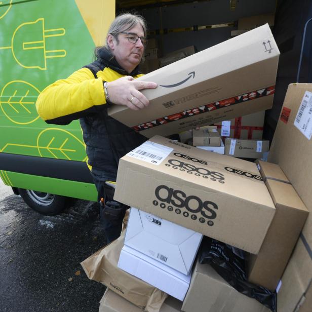 Ein Postbote entlädt Pakete von Amazon und ASOS aus einem gelben Lieferwagen.