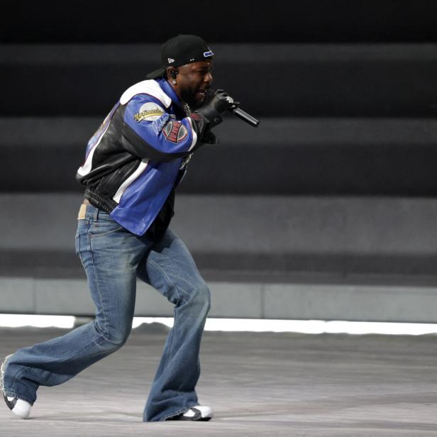 Der Rapper auf der Bühne mit bunter Lederjacke, Turnschuhen und weit ausgestellter Schlaghose.