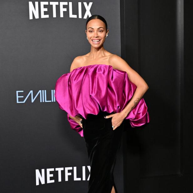 Zoe Saldaña in einem pinkfarbenen Oberteil und einem schwarzen Rock auf dem roten Teppich.