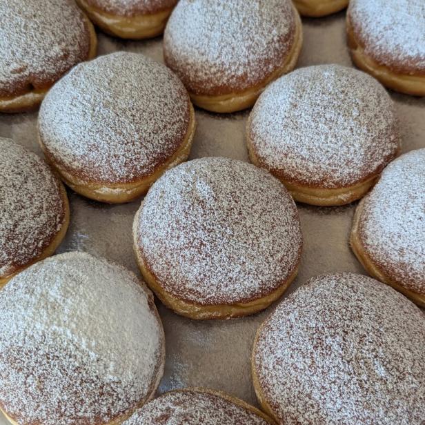 Mehrere Berliner Pfannkuchen, dick mit Puderzucker bestäubt, liegen auf einem Backblech.