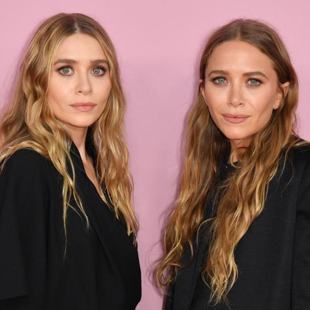 Die Zwillinge Mary-Kate und Ashley Olsen posieren vor einem rosa Hintergrund.