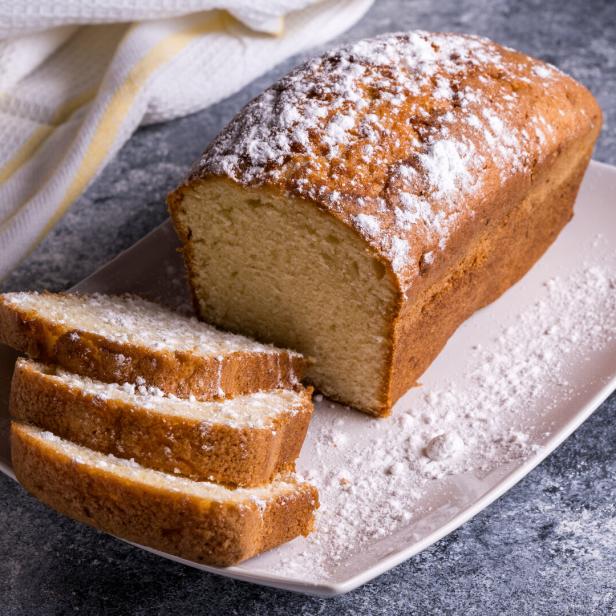 Ein Pfund Kuchen mit Puderzucker und angeschnittenen Stücken auf einem Teller.