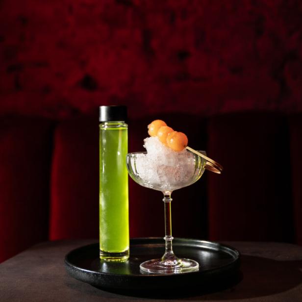 Ein Cocktail mit Melonenkugeln auf Eis und einer Flasche Limonade.