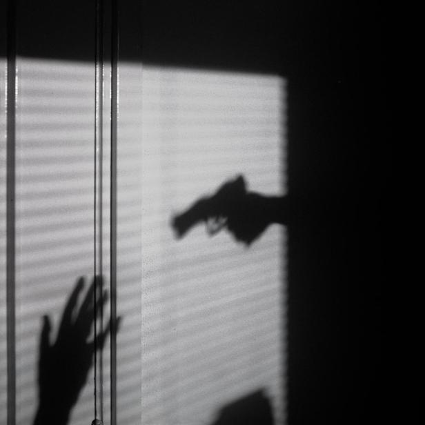 Ein Schatten von einer Pistole und einer Angegriffenen.