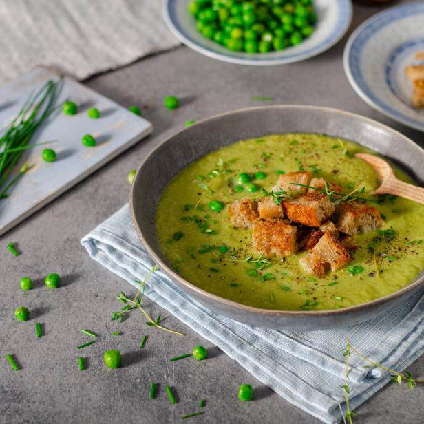 Eine Schüssel Erbsensuppe mit Croutons und frischen Kräutern garniert.