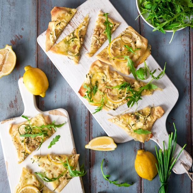 Flammkuchen mit Zitrone, Zucchini, Pinienkernen und Rucola auf Holzbrettern.