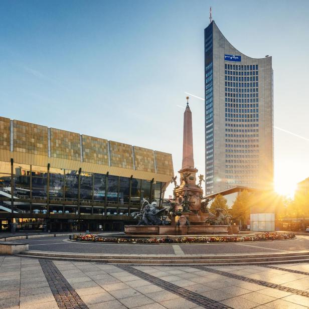 Ein Platz mit einem modernen Hochhaus, einem Brunnen und einem goldenen, verspiegelten Haus.
