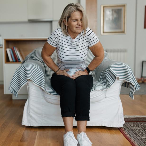 Eine Frau mit Blähungen und Magenschmerzen hält sich den Bauch.