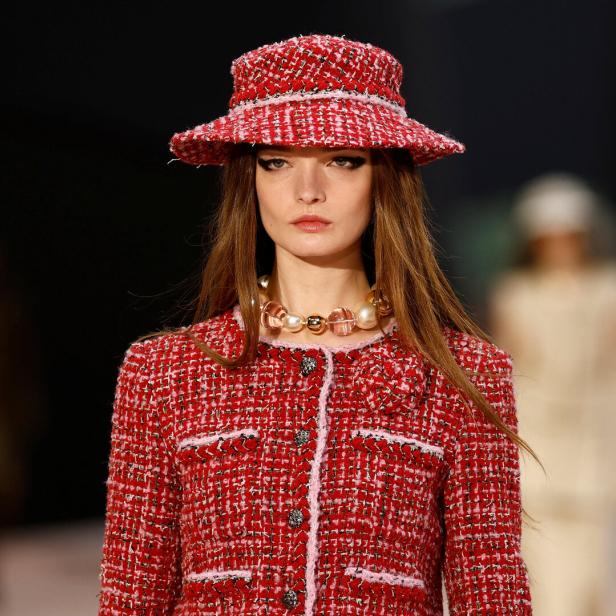 Ein Model mit rotem Tweed-Hut und passendem Blazer auf dem Laufsteg.