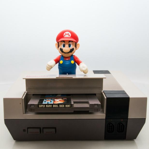 Eine Mario-Figur steht auf einer Nintendo-Konsole mit dem Spiel „Super Mario Bros./Duck Hunt“.