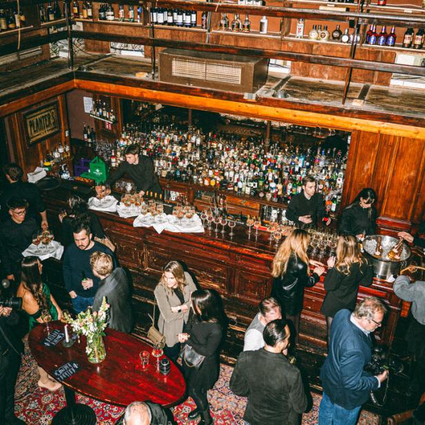 Blick von oben auf eine belebte Bar mit vielen Gästen und einer großen Auswahl an Spirituosen.