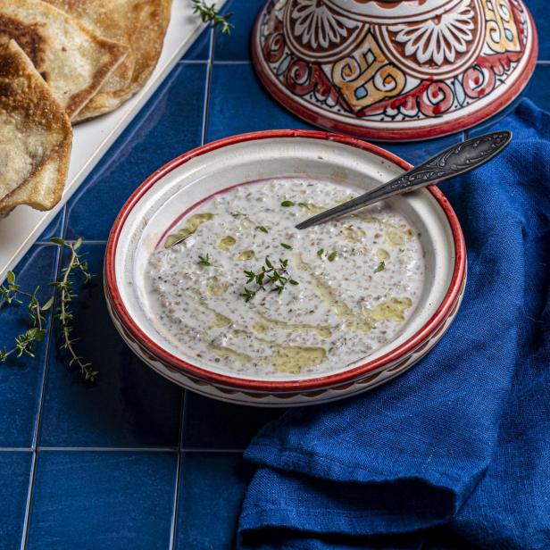 Eine Schüssel Gerstensuppe mit Brot und einem Tajine-Deckel auf blauem Fliesenhintergrund.