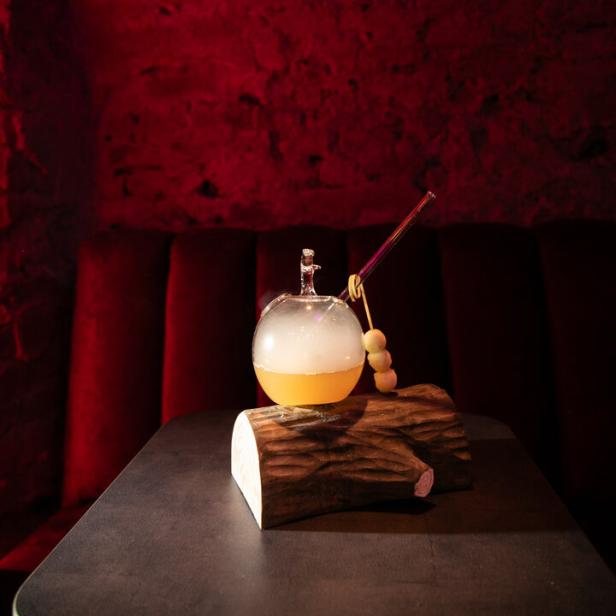 Ein Cocktail in einem Apfel-Glas auf einem Holzscheit, dekoriert mit Trockeneis.