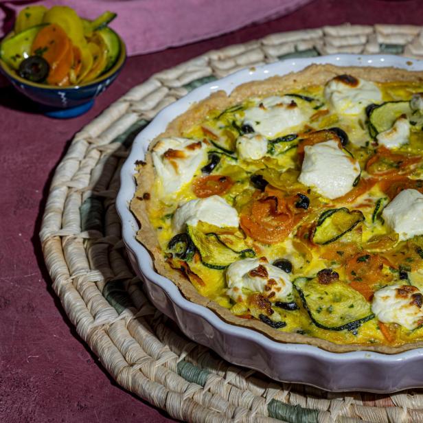 Eine Gemüse-Quiche mit Zucchini, Karotten und Käse in einer weißen Form.