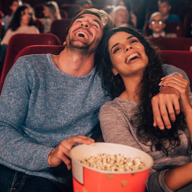 Ein lachendes Paar sitzt mit Popcorn im Kino.