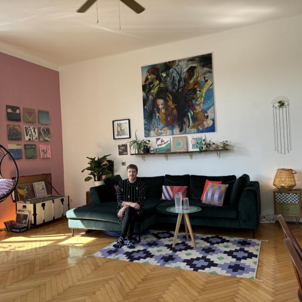 Ein Mann sitzt auf einem grünen Sofa in einem Wohnzimmer mit Kunstwerken und einem Hängesessel.