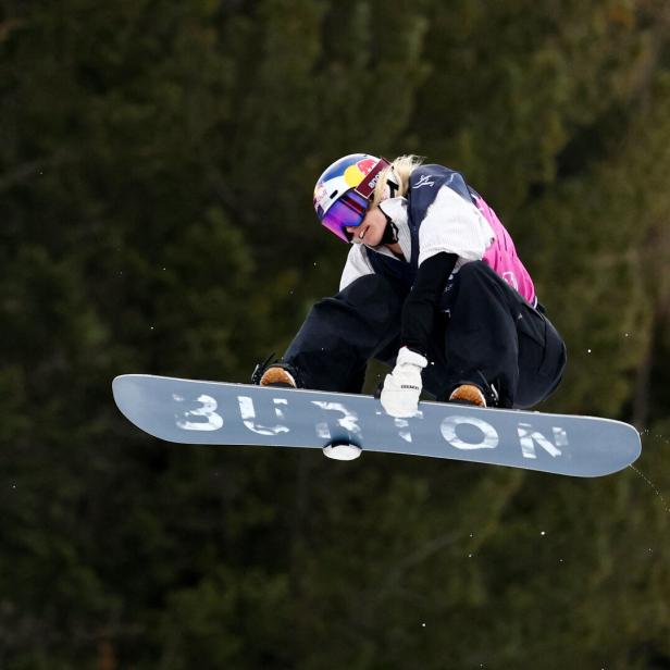 Eine Snowboarderin springt mit einem Burton-Snowboard vor einem bewaldeten Hintergrund.