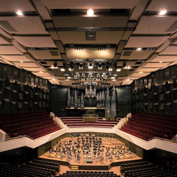 Blick in einen Konzertsaal mit Bühne, Orgel und rotem Gestühl.