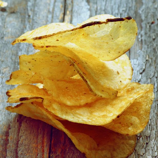 Ein Stapel goldgelber Kartoffelchips auf einem Holztisch.