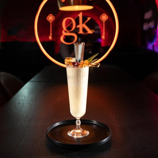 Ein Cocktail, möglicherweise eine Piña Colada, steht vor einem beleuchteten „glückskind“-Logo.