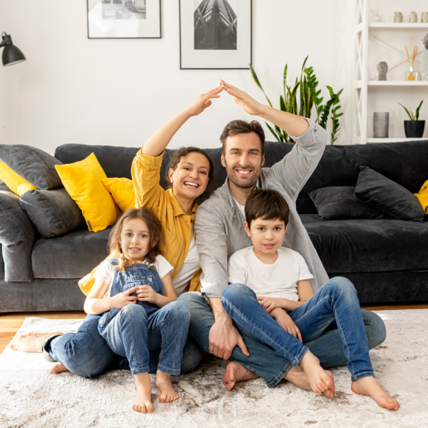 Eine vierköpfige Familie sitzt auf einem Teppich vor einem Sofa. 